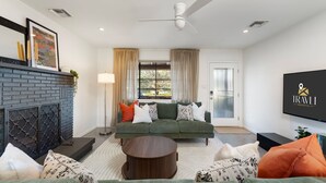 Un salon moderne avec un canapé vert, une cheminée, un ventilateur de plafond et un téléviseur affichant le logo « IRAVLI HOSPITALITY CO. »