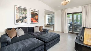 Un salon moderne avec un canapé d’angle, des œuvres d’art au mur, un coin repas et une grande fenêtre avec des rideaux.