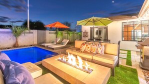Un jardin avec une piscine, un espace salon extérieur et un foyer.