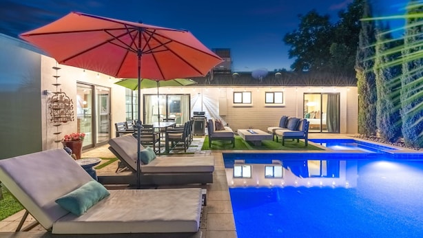 Un espace aménagé au bord de la piscine, avec des chaises longues, un parasol rouge et un bâtiment bien éclairé en arrière-plan.