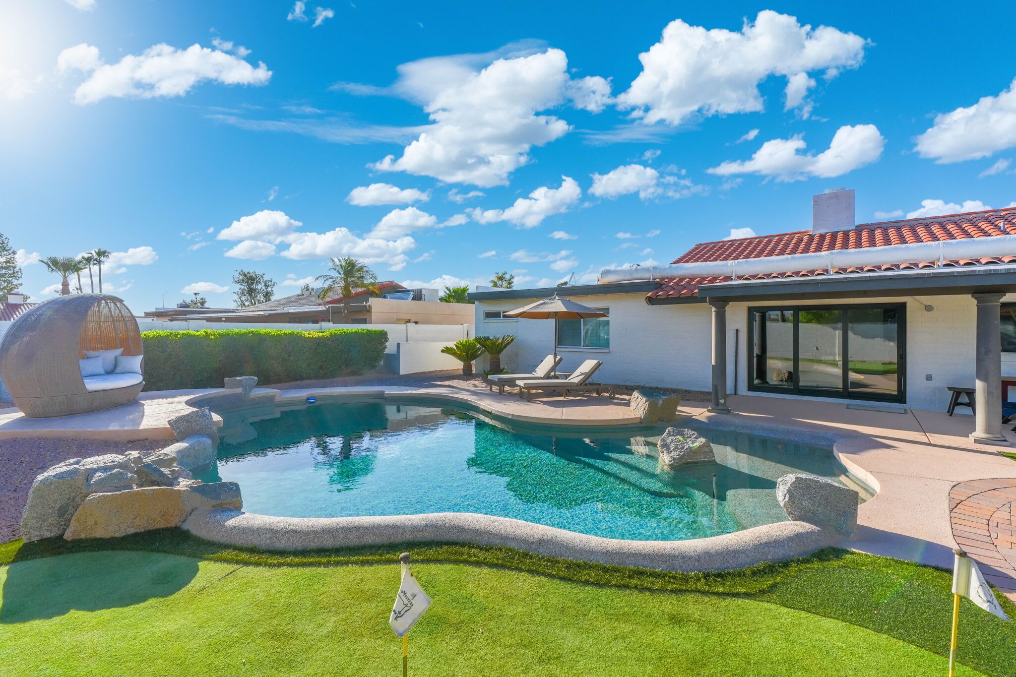 A modern house with a swimming pool, a covered patio, and a well-maintained lawn.