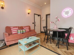 A cozy living room with a sofa, coffee table, and a dining area with chairs and a table. - Apartment Pink (Whitby)