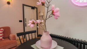 A dining table with a pink vase and magnolia flowers, a black chair, a pink sofa, and a wall-mounted light fixture. - Apartment Pink (Whitby)