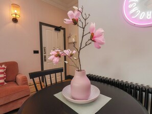 A dining table with a pink vase and magnolia flowers, a black chair, a pink sofa, and a wall-mounted light fixture. - Apartment Pink (Whitby)
