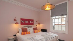 A bedroom with a bed, a window, a radiator, and a sign on the wall. - Apartment Pink (Whitby)