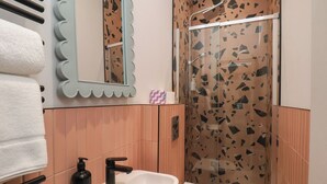 A bathroom with a white sink, black faucet, and a shower with a glass door. - Apartment Pink (Whitby)