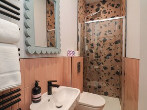 A bathroom with a white sink, black faucet, and a shower with a glass door. - Apartment Pink (Whitby)