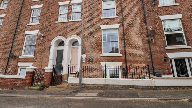 A red brick building with a white door, multiple windows, and a black metal fence. - Apartment Pink (Whitby)