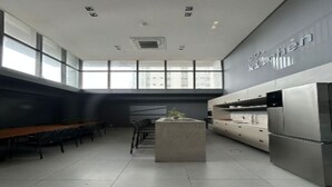 Une cuisine moderne équipée d’appareils électroménagers en acier inoxydable, un coin repas avec une longue table et de grandes fenêtres qui laissent entrer la lumière naturelle.