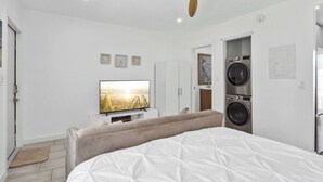 Un dormitorio con una cama, ventilador de techo, televisor, lavadora y una puerta que da a un baño.