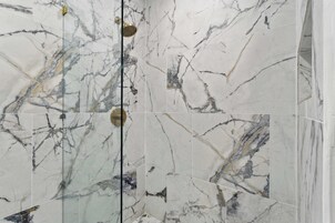 Un baño con baldosas de mármol y mampara de vidrio.