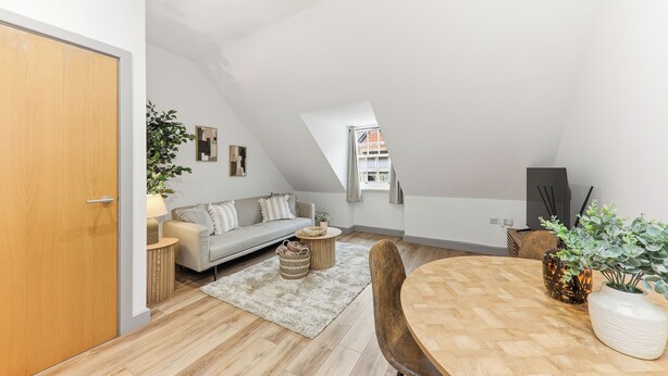 En modern lägenhet i loftstil med trägolv, en matplats med ett runt bord, en soffa och ett litet sidobord.