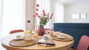 Une table ronde pour le petit-déjeuner, ornée d’un vase de fleurs, d’une carafe de jus d’orange et d’un bol de raisins.