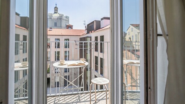 Un balcon avec une table et des chaises, une vue sur les bâtiments et un ciel dégagé.