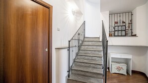 Une porte en bois, un escalier avec une rampe en métal, un mur blanc et une petite armoire blanche ornée de motifs floraux.
