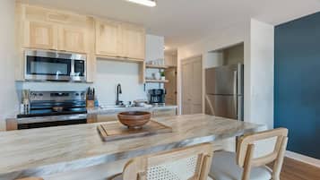 A modern kitchen with wooden cabinets, a marble countertop, a large island with chairs, a stainless steel refrigerator, and a microwave.