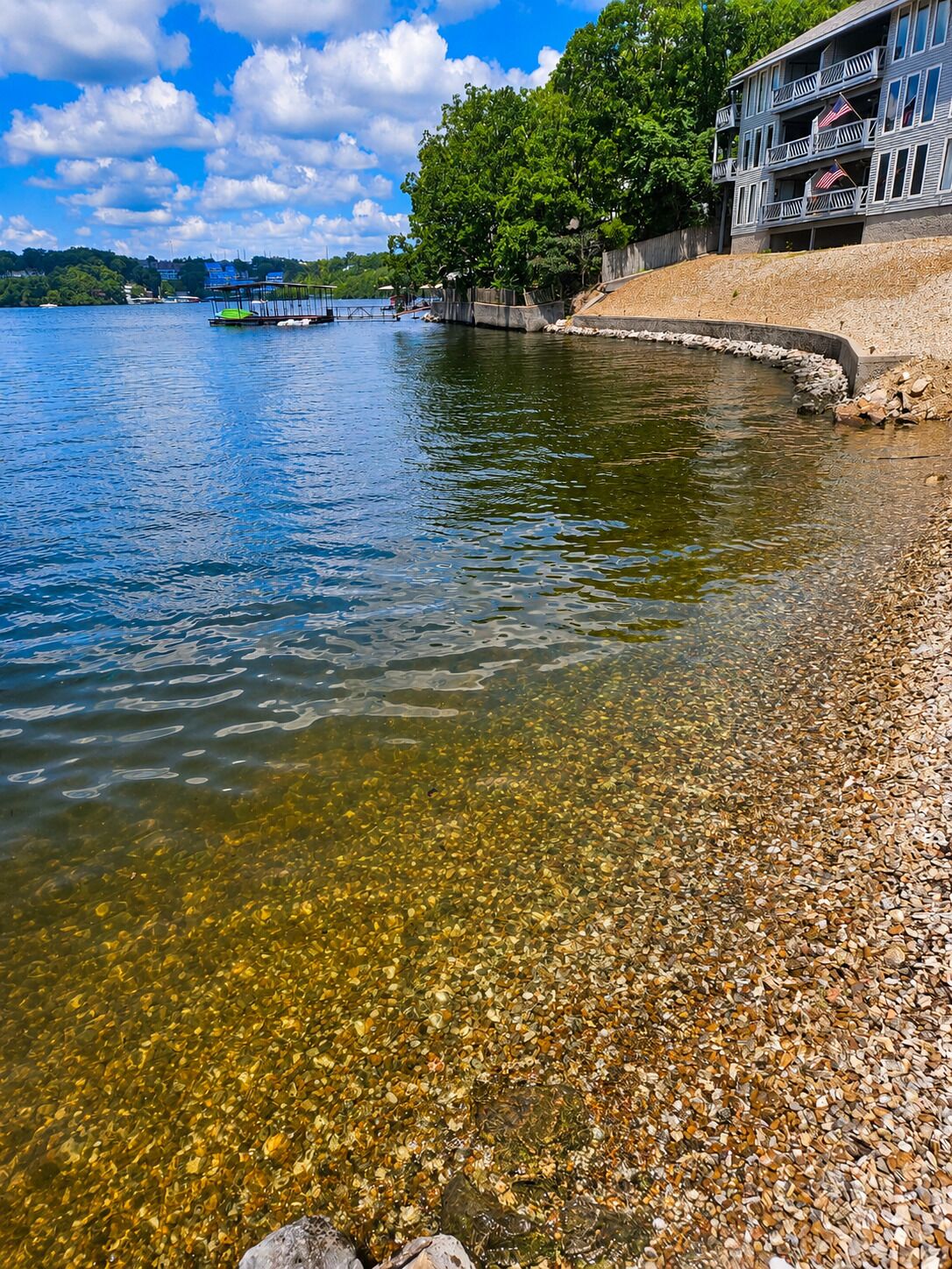 Un lac aux eaux limpides, des galets sur la rive et un bâtiment doté de balcons.
