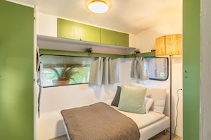 A compact bedroom with a bed, a window with curtains, a green cabinet above the bed, and a lamp on the right. - Tiny Home with Private Terrace on the Mönchgut Peninsula (Mönchgut)