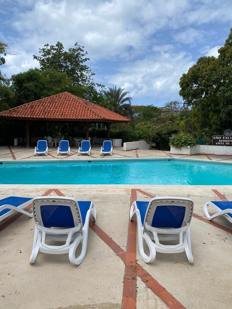 Un espace piscine avec des chaises longues, un pavillon couvert et un panneau indiquant : « USAGE EXCLUSIF POUR LES VISITEURS ».