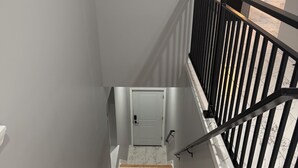 Una escalera con peldaños de madera y barandilla de metal negro, que conduce a una puerta blanca.