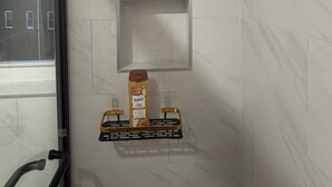 Un baño con baldosas de mármol blanco, una ventana y un estante con una botella y un recipiente.
