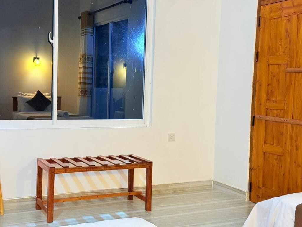 Una habitación con una cama, un banco de madera, una ventana y una puerta de madera.