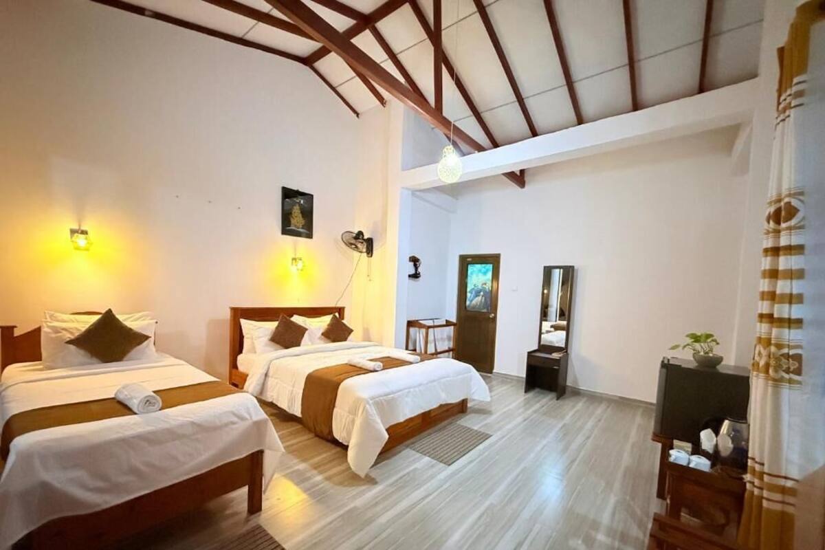 Habitación de hotel con dos camas, techo de madera, televisor de pantalla plana y una pequeña planta.