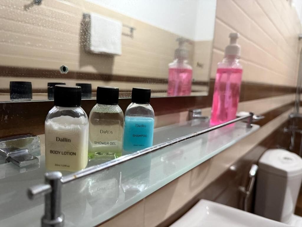 A bathroom with a mirror, three bottles of body lotion, a shower gel, and a shampoo bottle.
