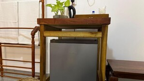 A compact refrigerator in a wooden frame, a wicker basket, and a plant on a table.