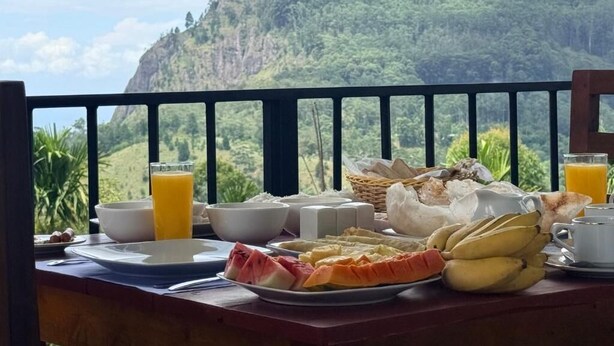 A breakfast table with a variety of food items and a glass of orange juice, set against a scenic mountain backdrop.