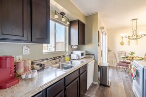 A kitchen with dark cabinets, a double sink, a microwave, and a dining area with a chandelier. - Tranquil Oasis Retreat. (Sierra Vista)