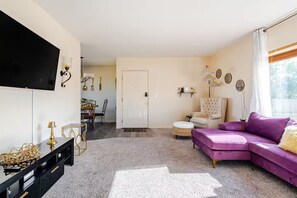 Un salon comprenant un canapé, un téléviseur et un coin repas avec des chaises et une table.