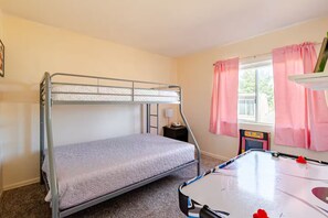 Une chambre avec un lit superposé, un bureau et une chaise, une fenêtre avec des rideaux et une petite table sur laquelle se trouve un jouet.