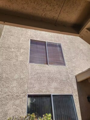 Une façade d’immeuble avec deux fenêtres, l’une dotée de stores horizontaux et l’autre de stores verticaux.