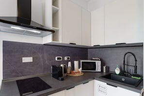 A modern kitchen with a black range hood, a microwave, a kettle, and a sink with a trash and recycle bin. - Room 'Camera Arsenale' with Wi-Fi and Air Conditioning (Venice)