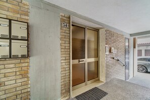 Une entrée d’immeuble avec une porte en verre, un mur en briques et un portail en métal.