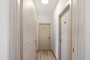 Un couloir étroit, avec des portes en bois de chaque côté, menant à une porte centrale dotée d’un trou de serrure et d’une sonnette.