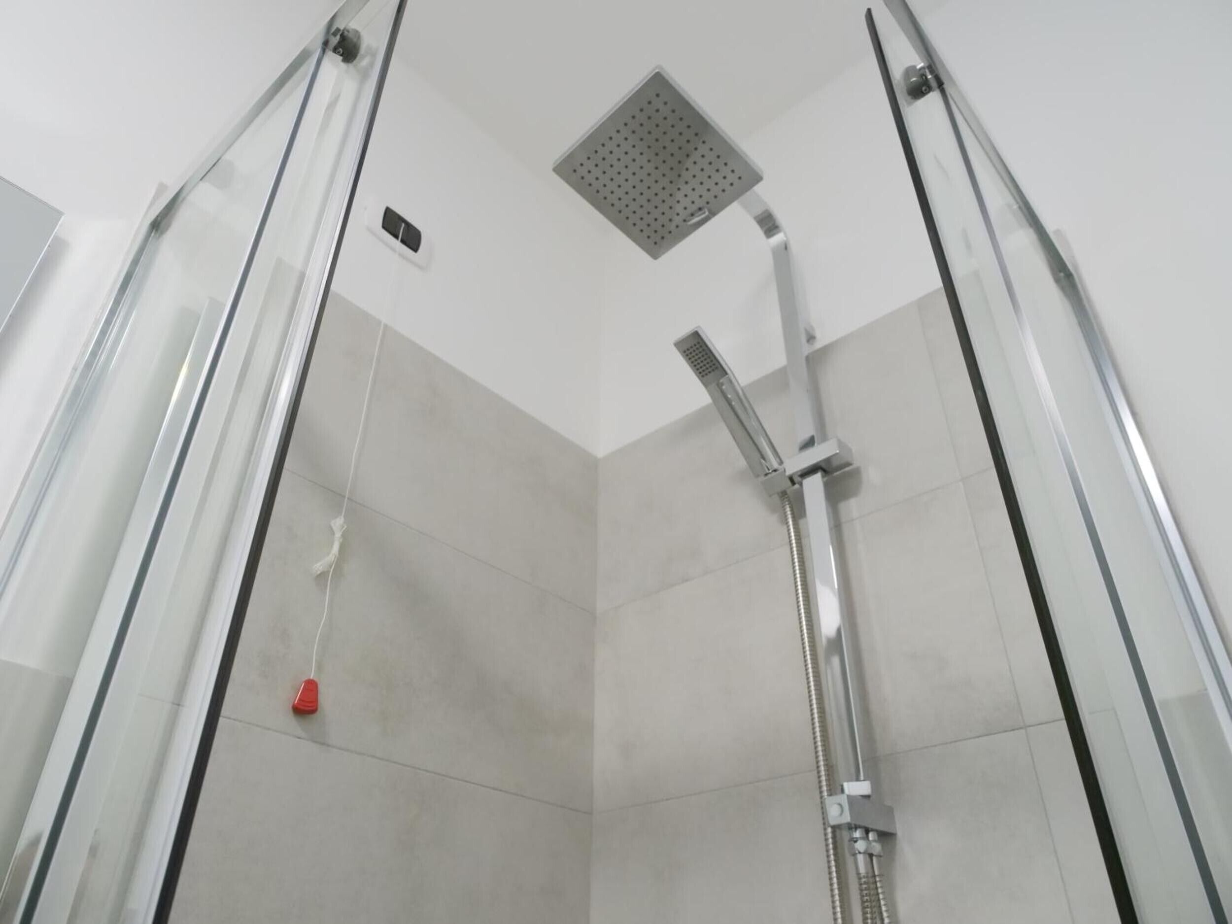 A shower with a handheld showerhead, a square ceiling vent, and a red object hanging from the ceiling.
