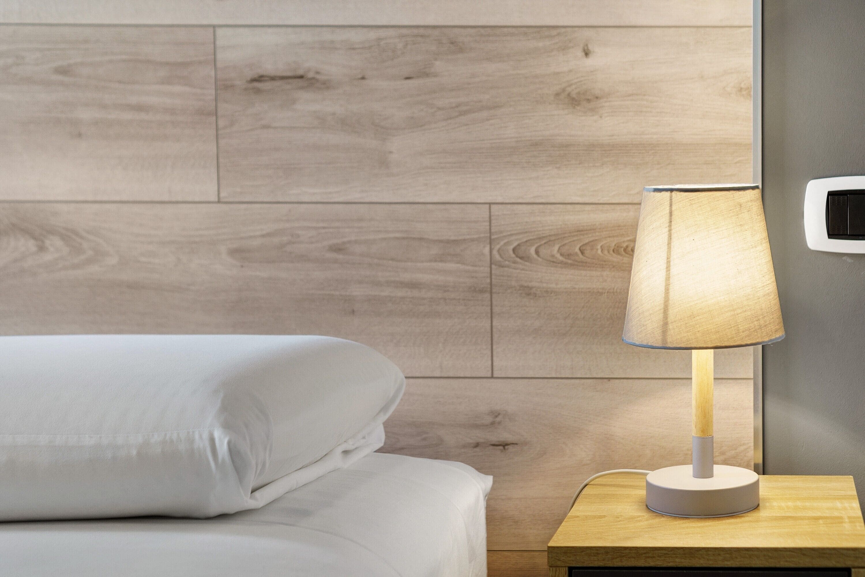 Un letto con biancheria bianca e un comodino con una lampada.
