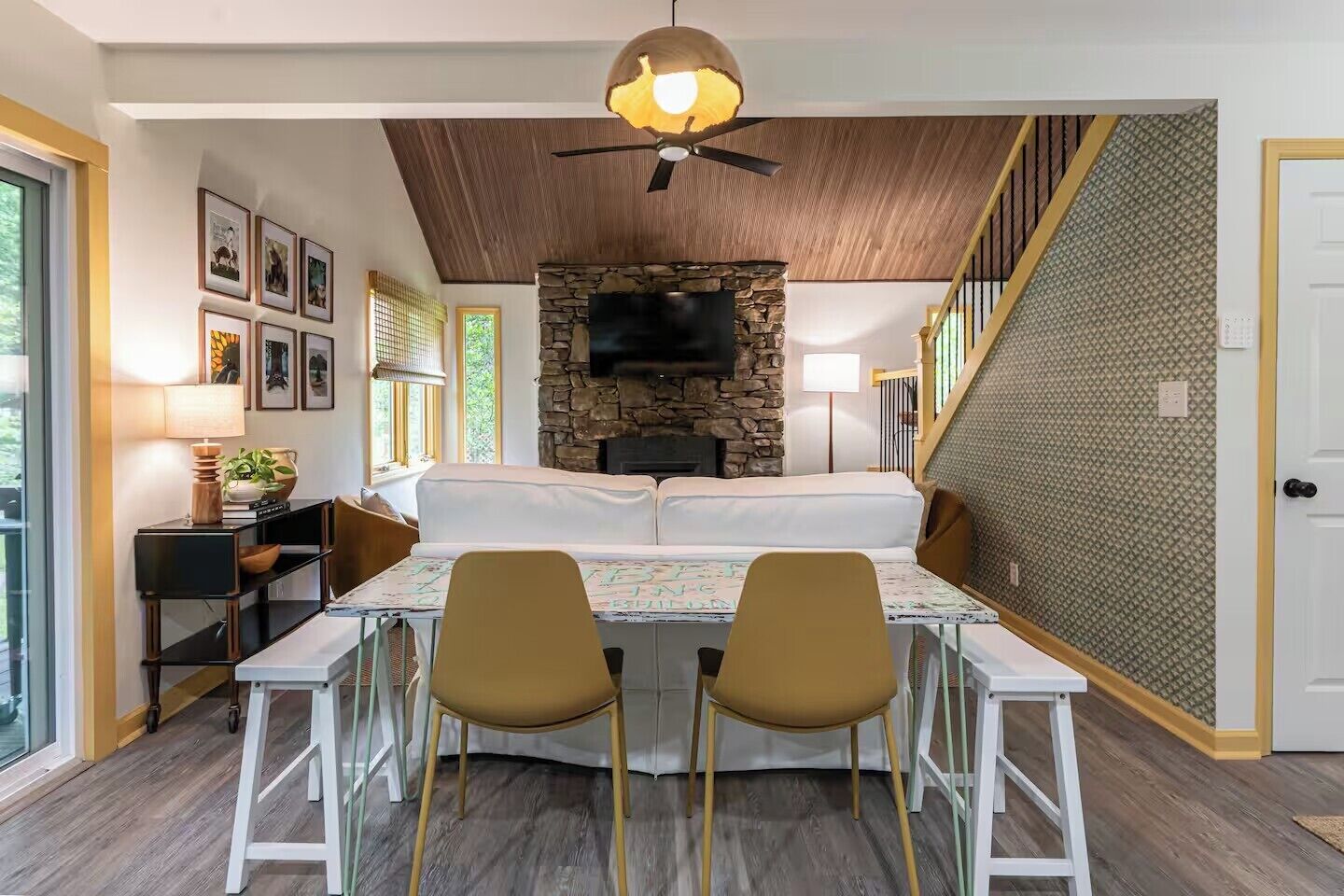 A cozy room with a stone fireplace, a dining table with chairs, and a TV mounted on the wall.