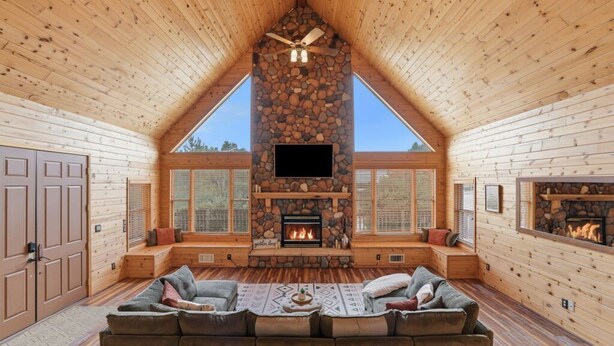L’intérieur d’une cabane en rondins, avec une cheminée en pierre, des murs en bois et une grande fenêtre.