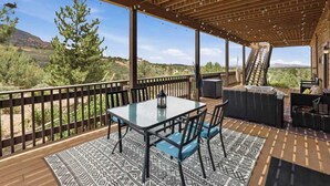 Une terrasse extérieure couverte, avec une table et des chaises, un escalier et une vue sur le paysage environnant.