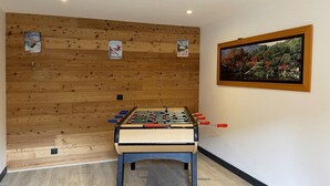 A room with a foosball table, wooden wall paneling, and a framed landscape painting. - Apartment - Le Batchu - Valloire - 12 guests (Valloire)