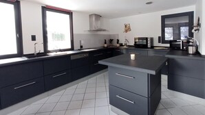 A modern kitchen with dark cabinetry, a large island, a microwave, and a stove. - Apartment - Le Batchu - Valloire - 12 guests (Valloire)