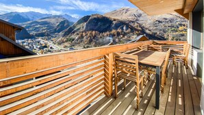 Terraza de madera con mesa y sillas, con vistas a un paisaje montañoso.