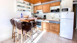 Una cocina con armarios de madera, un refrigerador blanco, un microondas, una cafetera y una mesa de comedor con sillas.