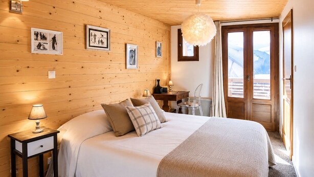 Una habitación acogedora con techo de madera, una cama con edredón blanco, un escritorio con silla y una ventana con vistas.