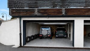 Un garaje con dos vehículos estacionados en su interior, un estante para neumáticos a la izquierda y una estructura de techo metálico.