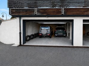 A garage with two vehicles parked inside, a tire rack on the left, and a metal roof structure above. - Apartment - Le Chaniski - Valloire - 4 guests (Valloire)