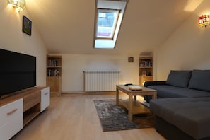 A modern living room with a sloped ceiling, built-in bookshelves, a flat-screen TV, a sofa, and a small table. - Stylish 1-Bedroom Apartment in Vračar Near Saint Sava Temple (Beograd)